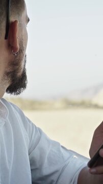 Caucasian man using cellphone inside car in a desert, sending text messages. Concept of people connected everywhere. Copy space vertical footage.