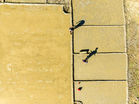 Aerial view of farmers working in muddy agricultural fields with long shadows cast on the ground in Cox's Bazar, Chittagong Division, Bangladesh.