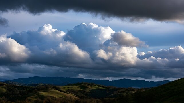 Dramatic cloud formations cast shadows over rolling green hills under a vast blue sky during daylight