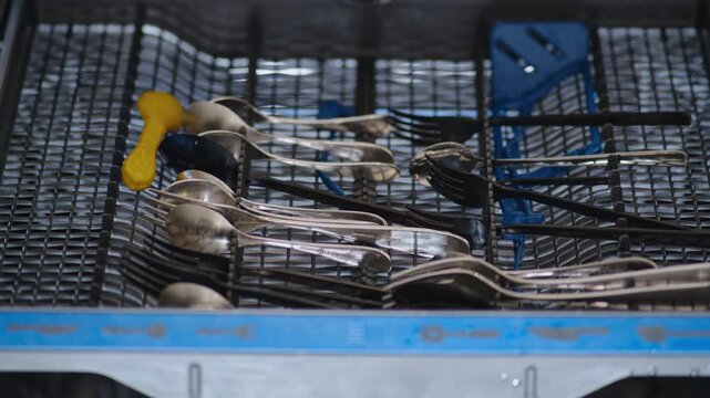 Loading dirty dishes into the dishwasher, stop motion. Filling the dishwasher with spoon, fork and knife