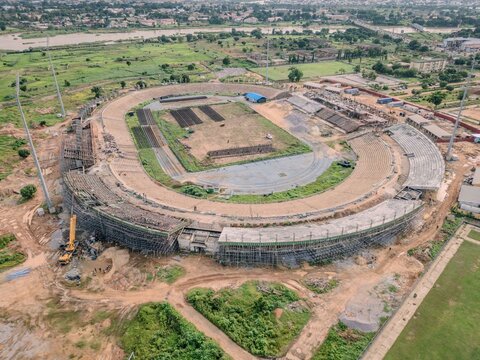 Aerial view of Ahmadu Bello Stadium under renovation with construction scaffolding on the seating areas, surrounding green fields, and urban landscape in Kaduna, Kaduna, Nigeria.