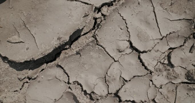 Panning shot of cracked dry mud and clay ground in arid riverbed basin during drought, top view.