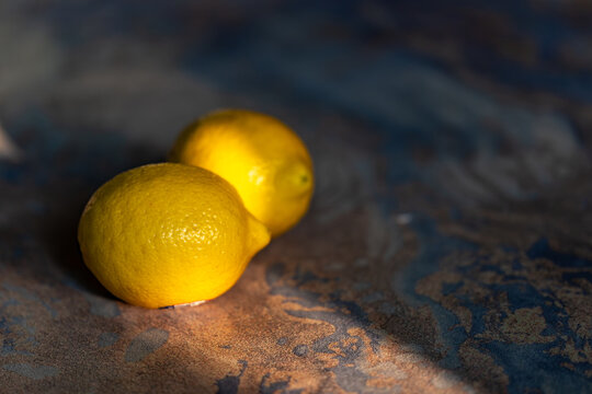 Still life close-up of two fresh yellow lemons against a dark background and under a single light source.
