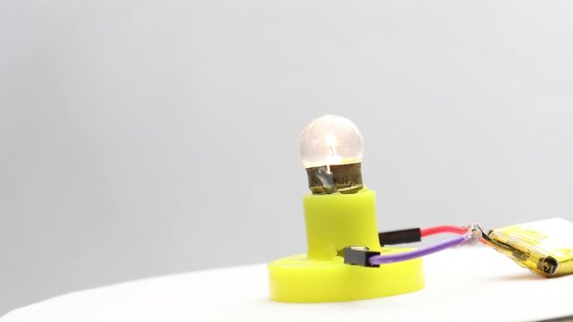 Small incandescent light bulb glowing rotating on a display stand connected to a small battery
