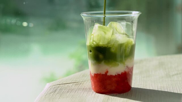 A cinematic close-up shot of pouring vibrant green matcha tea over milk and fresh strawberry puree in a glass cup filled with ice cubes