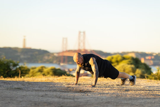 Man doing push-ups near a bridge in a scenic location during sunset hours
