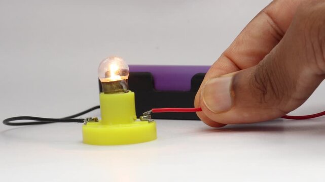 Small incandescent bulb glowing using power from a lithium polymer battery connected to a battery holder