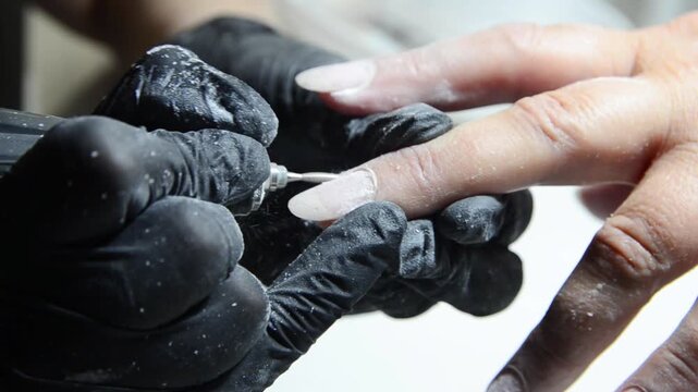 Professional manicurist removing cuticle with an electric nail drill during a hardware manicure. Close-up of nail preparation and cuticle care in a beauty salon.