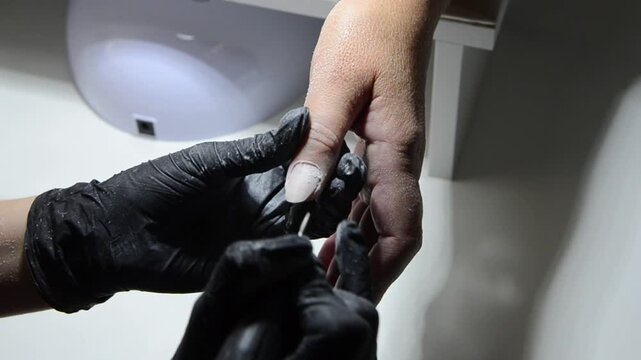 Professional manicurist removing cuticle with an electric nail drill during a hardware manicure. Close-up of nail preparation and cuticle care in a beauty salon.