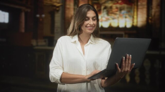 Woman holding laptop with hands, typing and smiling in ornate church building near stained glass altar; remote work serenity.