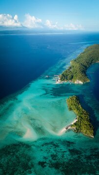 Aerial view of Raja Ampat Regency islands with lush green vegetation, turquoise waters, coral reefs, and overwater bungalows in Waigeo Barat Kepulauan, Southwest Papua, Indonesia.