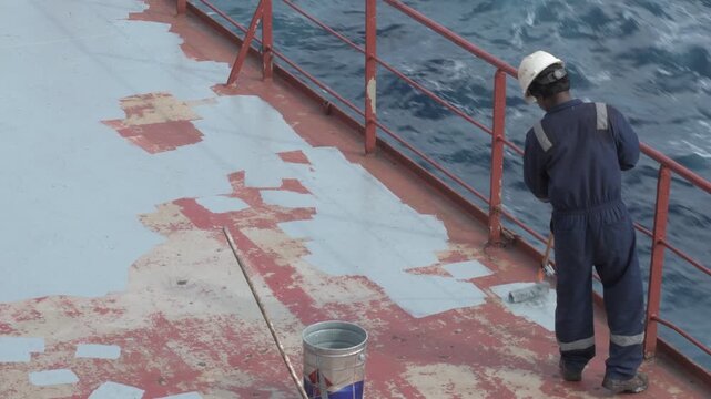 manual applying of protective deck coating on a cargo ship while underway at sea