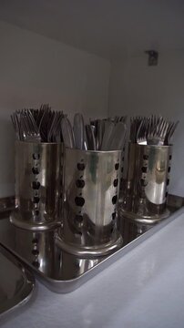 Close up of stainless steel cutlery holders filled with forks and knives on a metal tray inside a kitchen cabinet, slow motion vertical video.