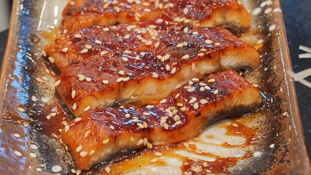 Grilled unagi kabayaki freshwater eel glazed with sweet soy tare sauce and toasted sesame seeds on a rustic ceramic plate