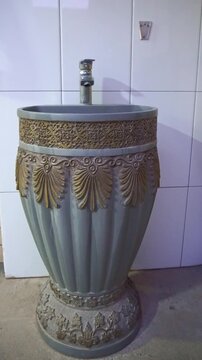 Slow motion camera panning of a decorative luxury pedestal sink with oriental gold ornaments and a classic chrome faucet, vertical video.