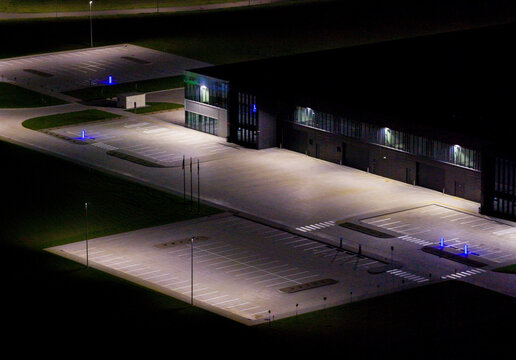 Aerial view of a modern industrial building illuminated at night with empty parking lots and surrounding green spaces in Vilnius, Vilnius County, Lithuania.