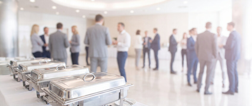 Catering buffet table at a business event featuring stainless steel chafing dishes on a white tablecloth, ideal for corporate reception, conference, and banquet stock concepts