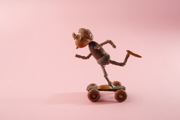 Handmade acorn figurine skateboarding on pink background. Great for kids toy stores, craft shops, educational blogs, and autumn design projects © Elena