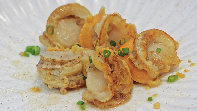 Grilled Hokkaido scallops with roe in butter garlic sauce topped with chopped spring onion, served on a white ceramic plate