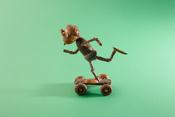 Creative autumn craft project featuring miniature acorn skateboarder on green background. Ideal for DIY blogs, art studios, and hobby stores selling natural material crafting kits © Elena