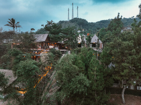 Aerial view of a rustic wooden resort nestled among lush pine trees and dense forest in the hilly landscape of Pasirjambu, West Java, Indonesia.