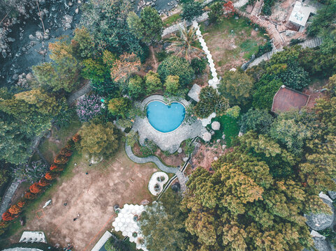 Aerial view of a heart-shaped swimming pool surrounded by lush trees, walking paths, and landscaped grounds in Pasirjambu, West Java, Indonesia.