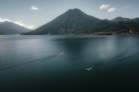 Aerial view of Lake Atitlan with small boats traversing the deep blue water, framed by the majestic volcanic peaks of the highlands in Solola Department, Guatemala.