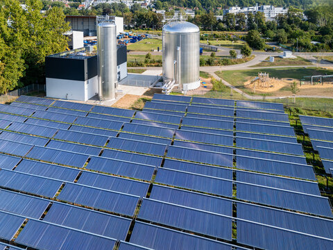 Aerial view of a solar thermal plant featuring rows of solar collectors and large metal storage tanks situated in a green area in Germany.