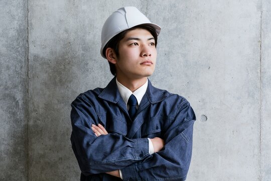 建設業で働く若い日本人男性技術者が腕組みし真剣な表情で未来を見据える
