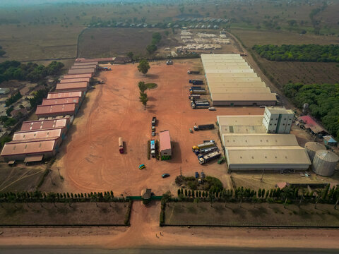 Aerial view of an industrial logistics facility with warehouses, parked trucks, and a large dirt yard along the Abuja - Kaduna - Zaria Express Way in Kaduna, Kaduna, Nigeria.