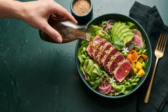 Seared Ahi tuna salad bowl with avocado, edamame, sesame dressing, bottle, fork, and hand-poured dressing