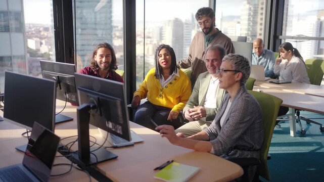 Diverse group gathers around a screen for a collaborative discussion as a middle aged businesswoman leads the conversation sharing ideas guiding colleagues during a strategy meeting in a modern office
