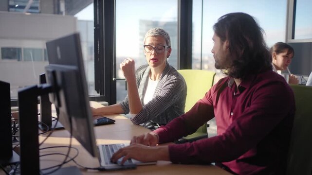Male and female colleagues collaborating on a computer project in a bright modern office with natural light, showing teamwork, communication and cooperation.