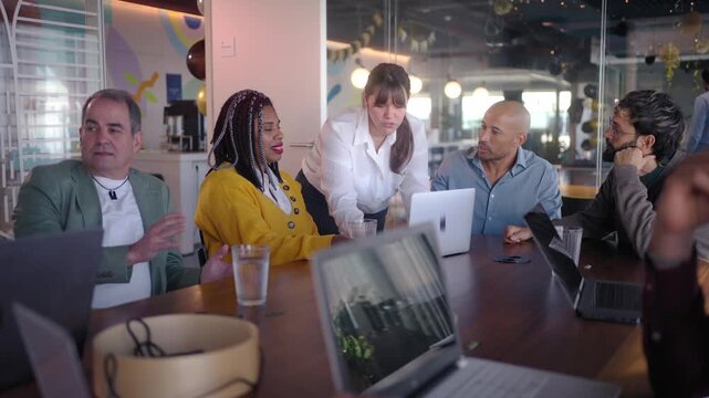 Businesswoman leading a discussion with diverse colleagues gathered around a laptop in a modern office. Professional scene conveying communication, planning and collaborative decision making.