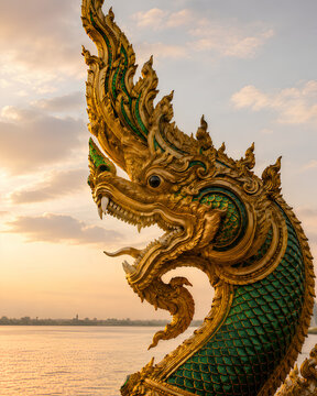 Golden Naga serpent statue by the river at sunset