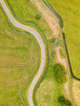Aerial view of the winding road at Busch en Dam surrounded by lush green pastures and drainage canals in Uitgeest, Noord-Holland, Netherlands.