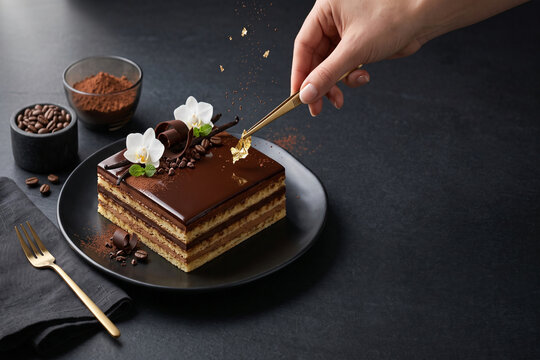 French opera cake plate with coffee beans, cocoa powder, tweezers, dark background, and hand-placed gold leaf