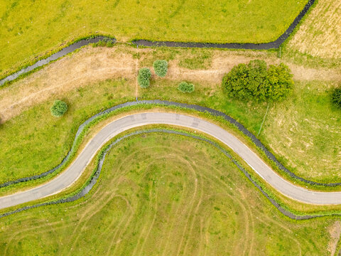 Aerial view of the winding road and canal at Busch en Dam surrounded by lush green fields in Uitgeest, Noord-Holland, Netherlands.
