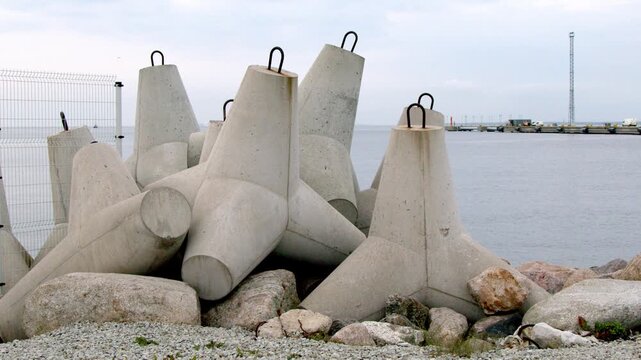 Massive concrete breakwater armor units stacked along a harbor shoreline to protect coastal infrastructure from waves and erosion. Static close-up of marine engineering structures beside calm sea