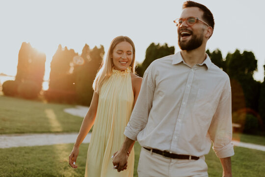 Couple walks hand in hand during sunset in a park with green grass and trees