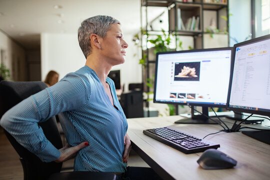 Mature woman suffering back pain at office desk