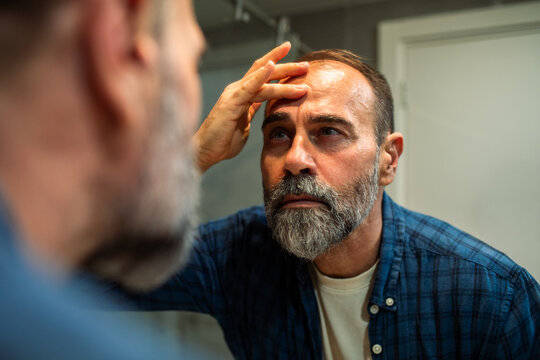 Middle-aged man checking forehead wrinkles in bathroom mirror