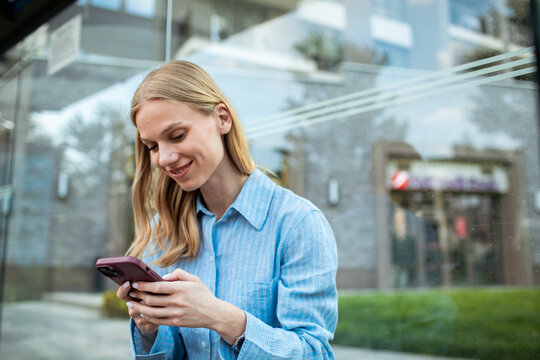 Smiling young woman using smartphone at city bus stop