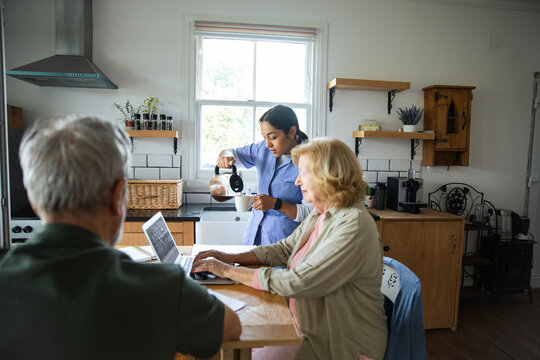 Caregiver pouring coffee for senior couple at kitchen table