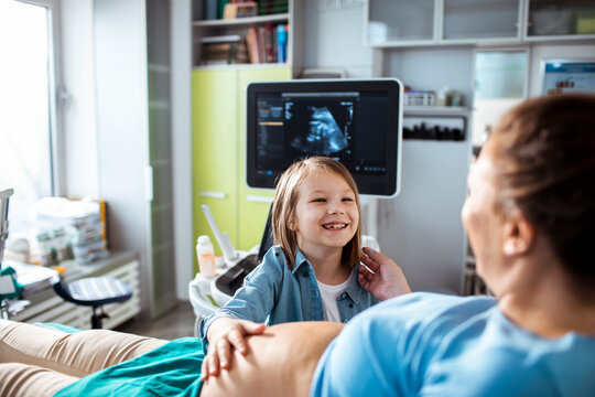 Smiling child with pregnant mother during ultrasound exam in clinic