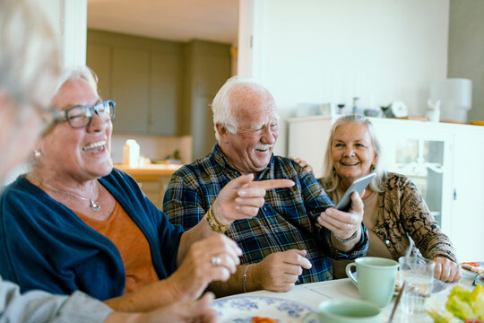 Senior friends laughing over smartphone at kitchen table