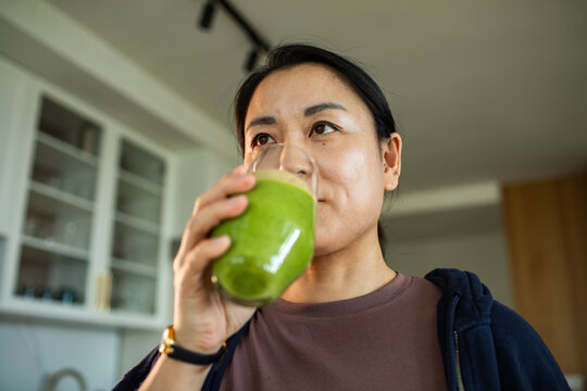 Woman drinking green smoothie in kitchen
