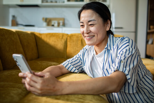 Smiling woman using smartphone on sofa at home