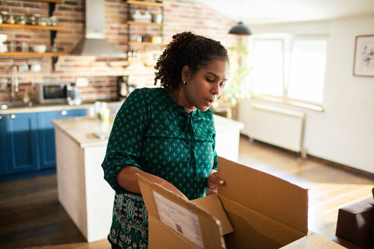 Woman unboxing delivery package in home kitchen