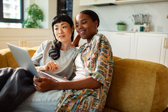 Two women relaxing with laptop on sofa at home